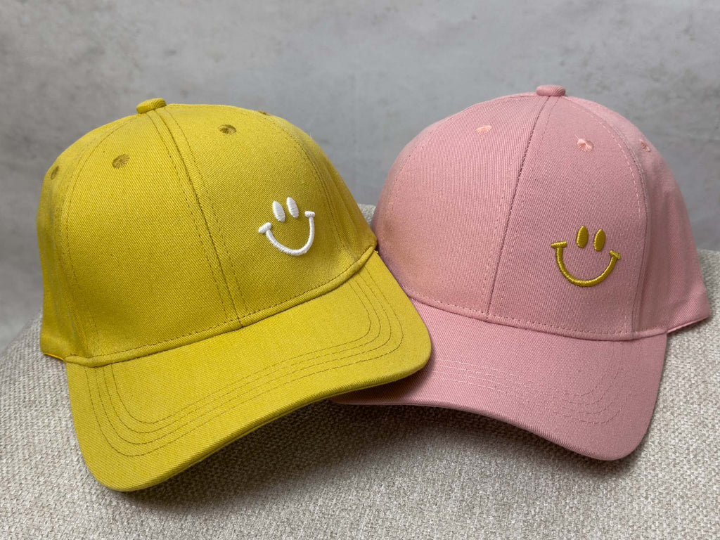Zwei Baseball Caps in Senfgelb und Rosa mit gesticktem Smiley Motiv