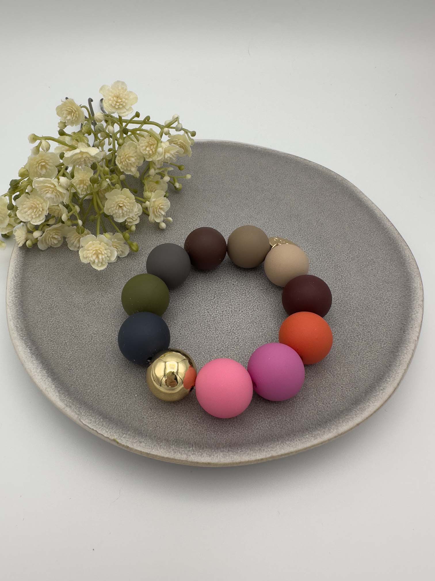 Elastisches Armband mit bunten matten Perlen in Pink, Lila, Orange, Gruen und Blau sowie einer grossen goldenen Kugel