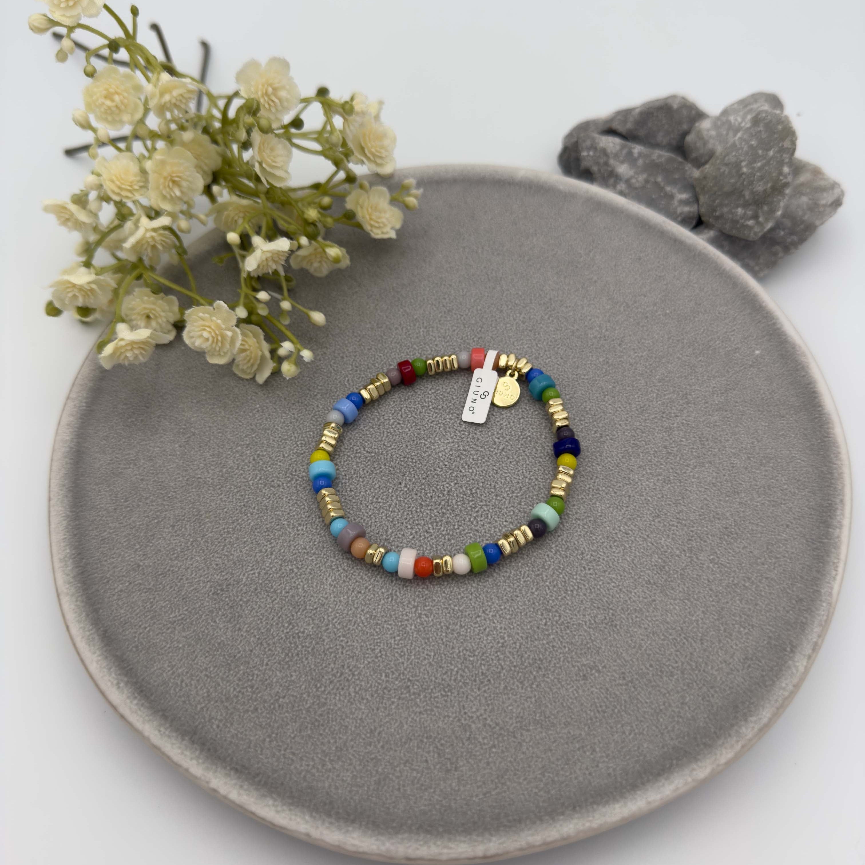 Elastisches Armband mit vielfarbigen runden Perlen in Blau, Gruen, Rot, Gelb und weiteren Toenen, kombiniert mit goldfarbenen Zwischenelementen und kleinen Anhaengern.
