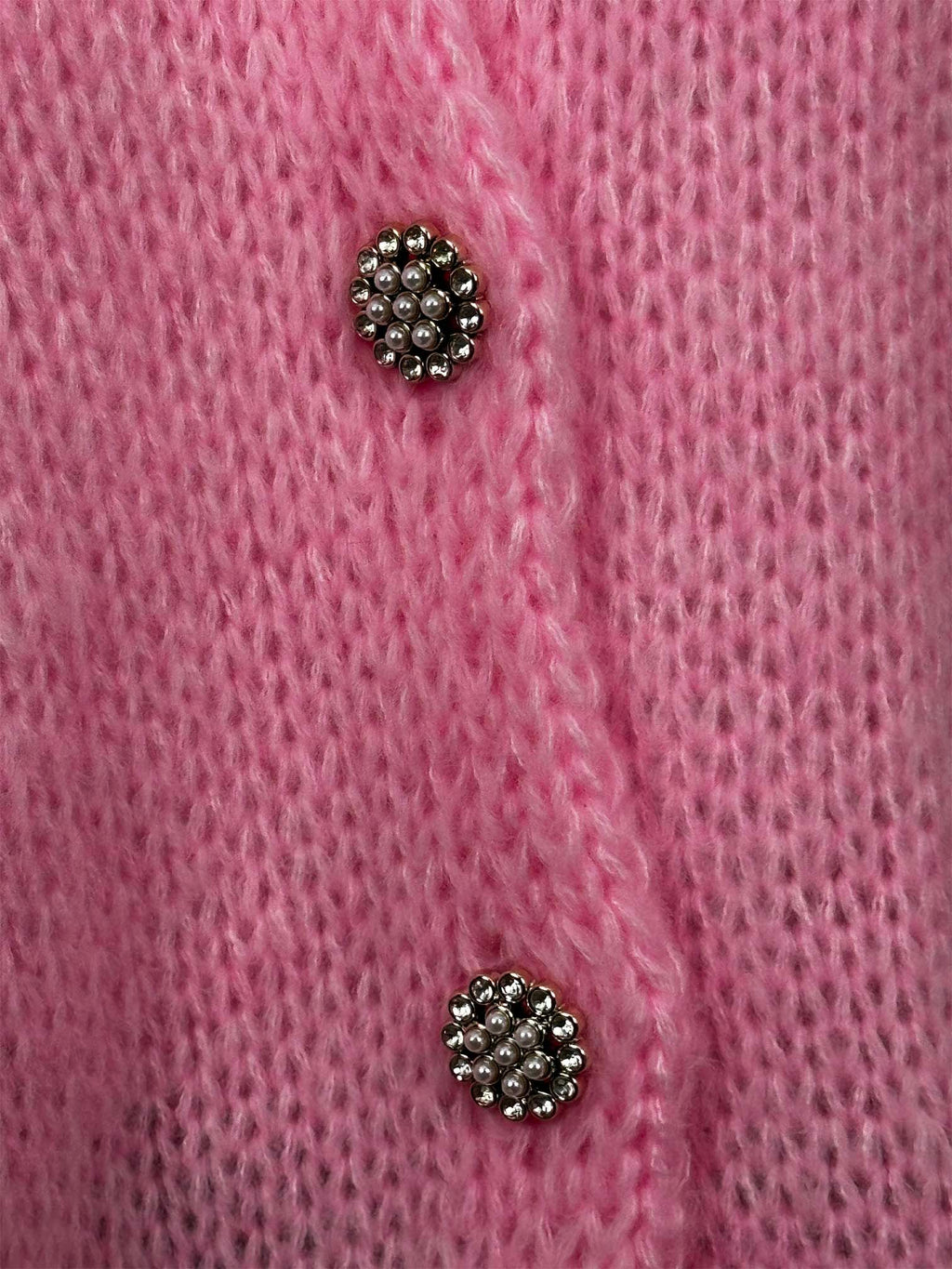 Detailaufnahme von funkelnden Schmuckknöpfen auf rosa Strickjacke