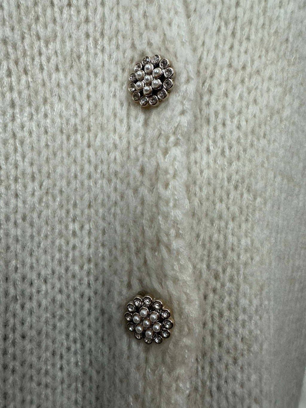Detailaufnahme von funkelnden Schmuckknöpfen auf creme Strickjacke
