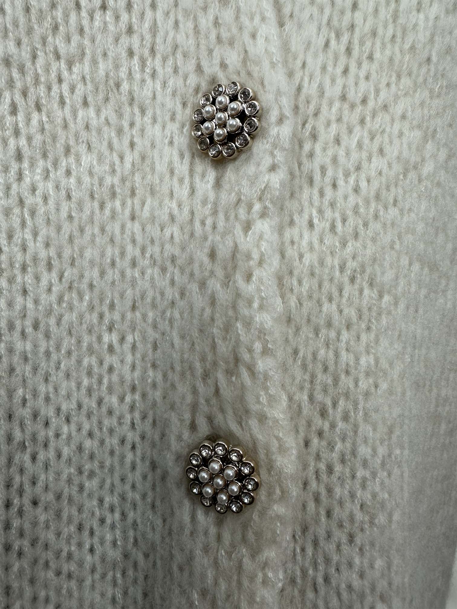 Detailaufnahme von funkelnden Schmuckknöpfen auf creme Strickjacke