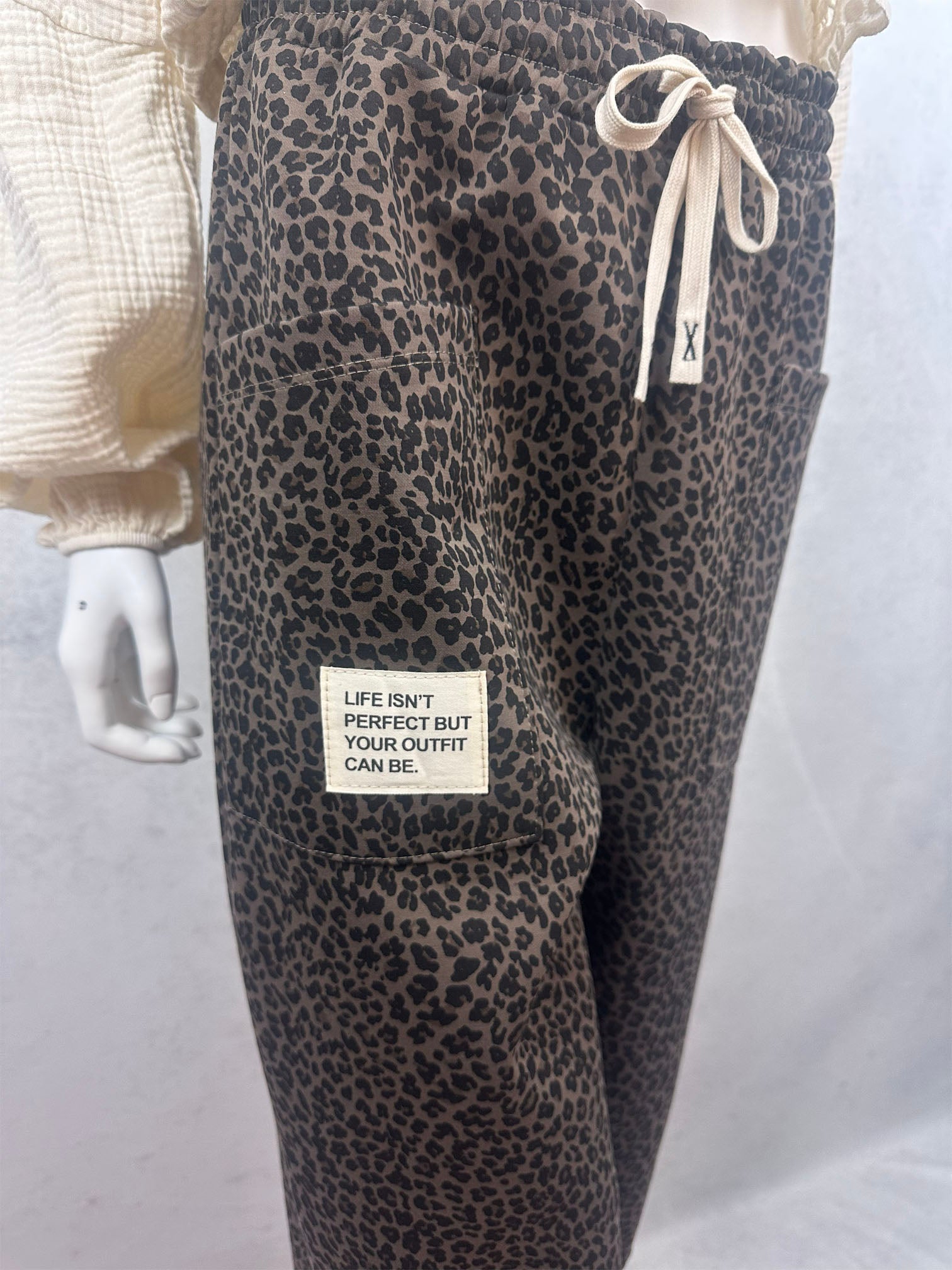 Dunkelbraune Leo Hose mit feinem schwarzen Leo Muster, grosser aufgesetzter Tasche und hellem Stoffpatch mit dem Schriftzug Life isnt perfect but your outfit can be sowie elastischem Bund mit Kordel