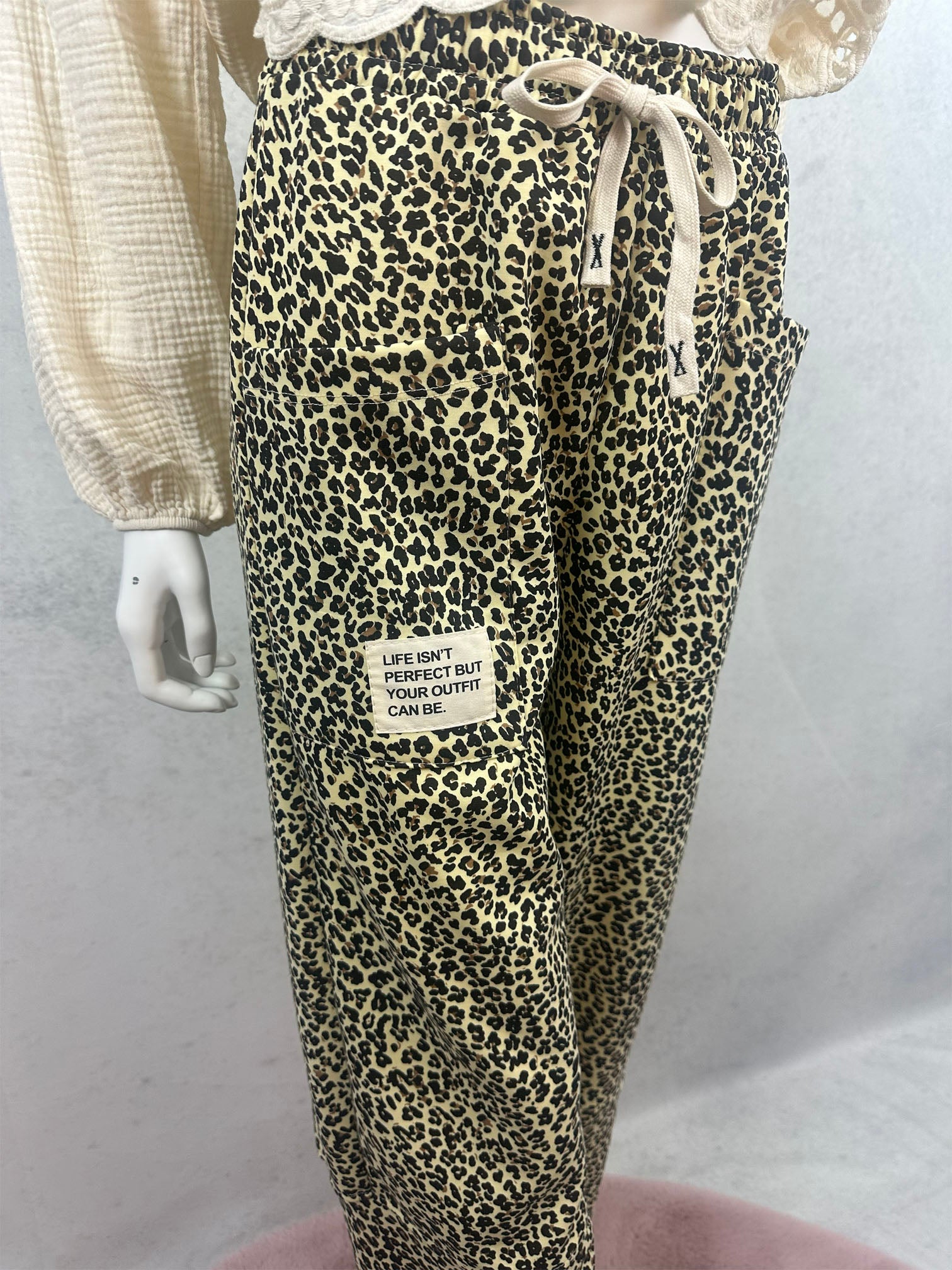 Gelbe Leo Hose mit schwarzem Leo Muster, grosser Fronttasche und hellem Patch mit dem Text Life isnt perfect but your outfit can be sowie elastischem Bund mit Kordelzug
