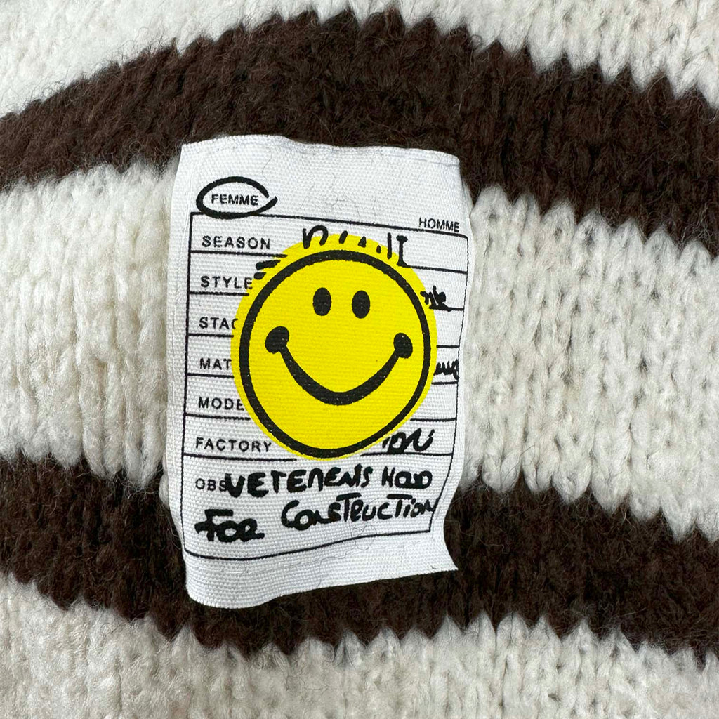Nahaufnahme des Smiley Labels auf gestreiftem Cardigan