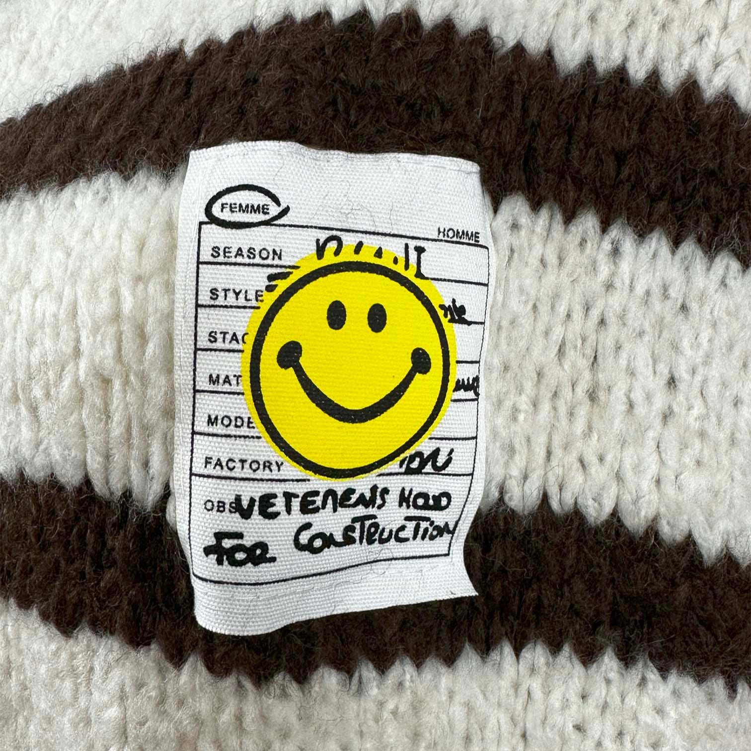 Nahaufnahme des Smiley Labels auf gestreiftem Cardigan