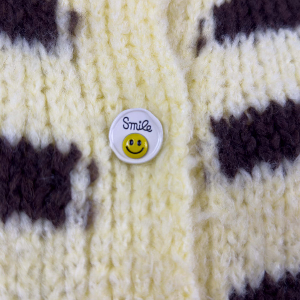 Nahaufnahme eines runden weissen Knopfes mit Smiley Motiv auf gelb braun gestreiftem Strickcardigan