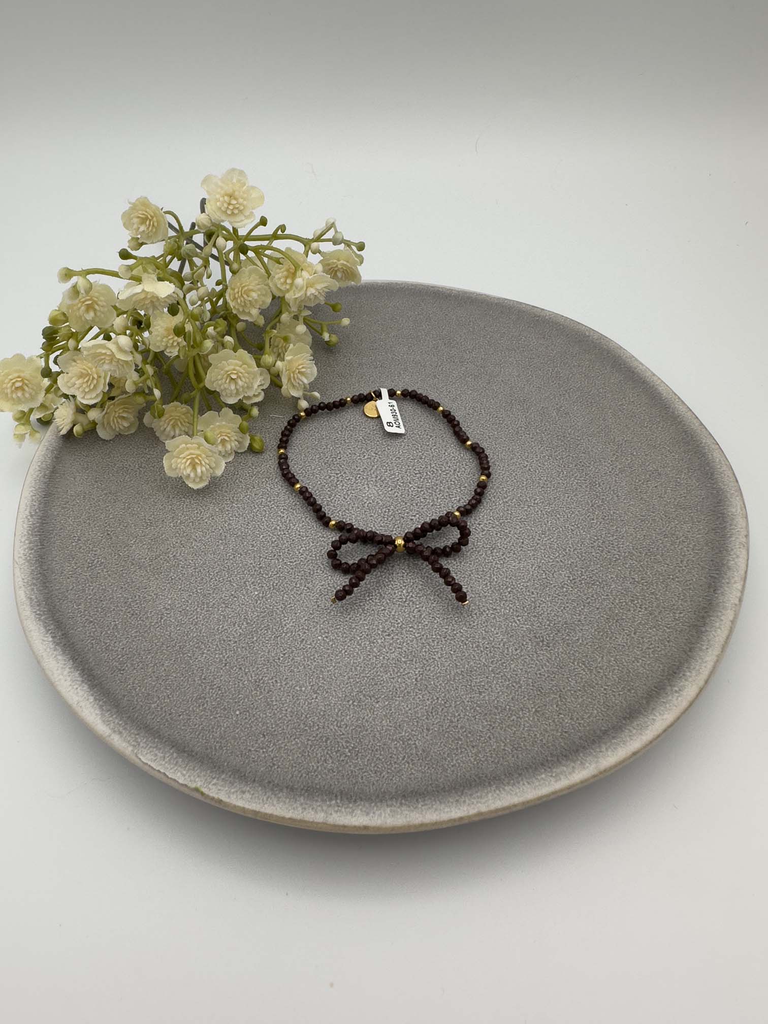 Elastisches Armband aus dunkelbraunen Perlen mit goldfarbenen Details und Schleife