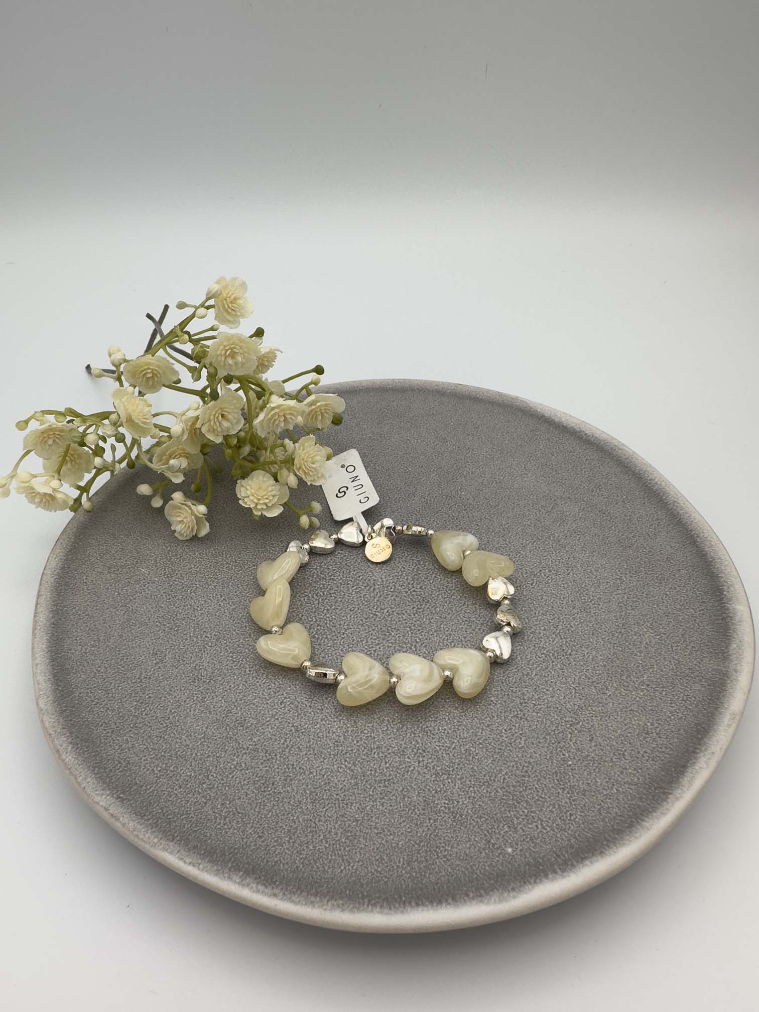 Cremefarbenes Armband mit Herzperlen und silberfarbenen Details.
