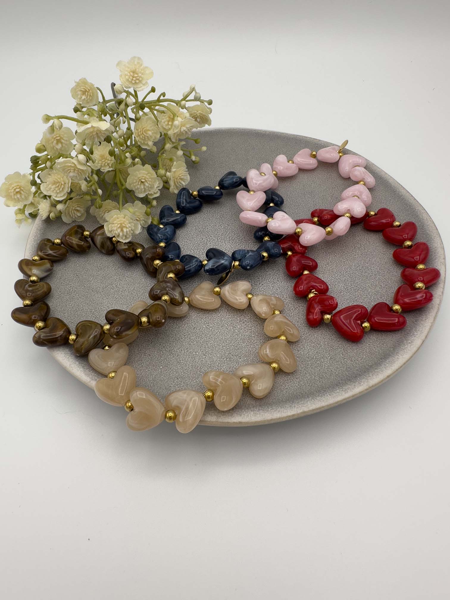 Elastisches Armband mit herzfoermigen Perlen in verschiedenen Farben und goldfarbenen Kugeln als Akzent