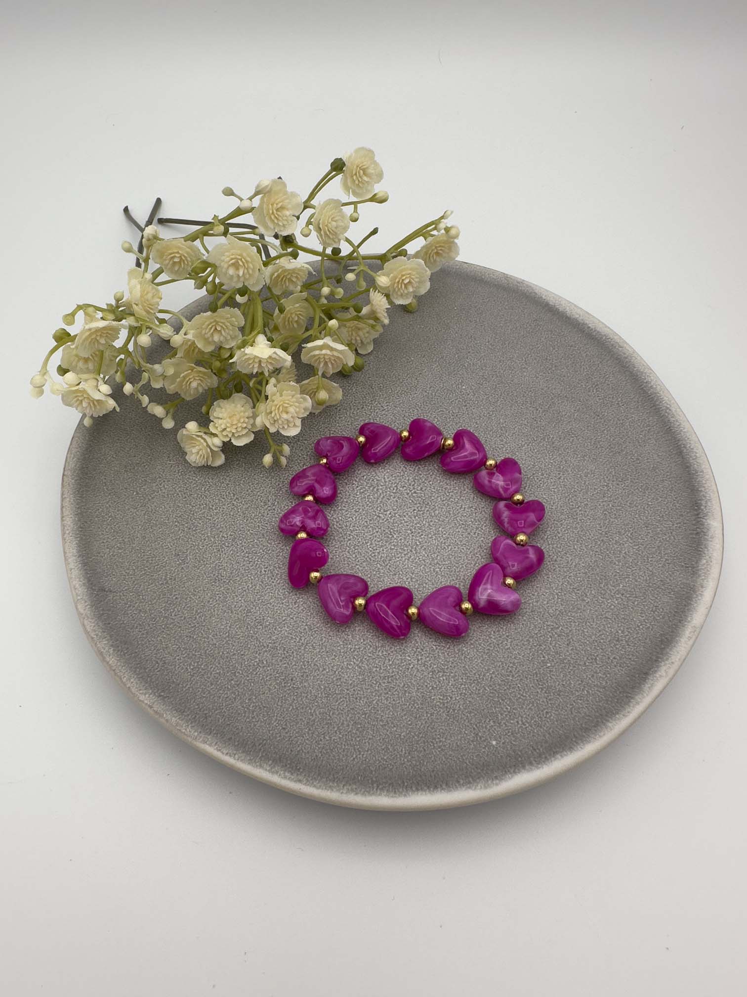 Pinkes Armband mit herzfoermigen Perlen und goldfarbenen Kugeln auf elastischem Band