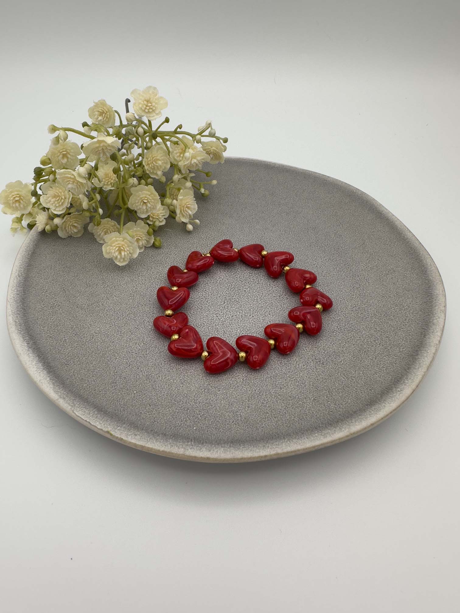 Rotes Armband mit herzfoermigen Perlen und goldfarbenen Kugeln auf elastischem Band