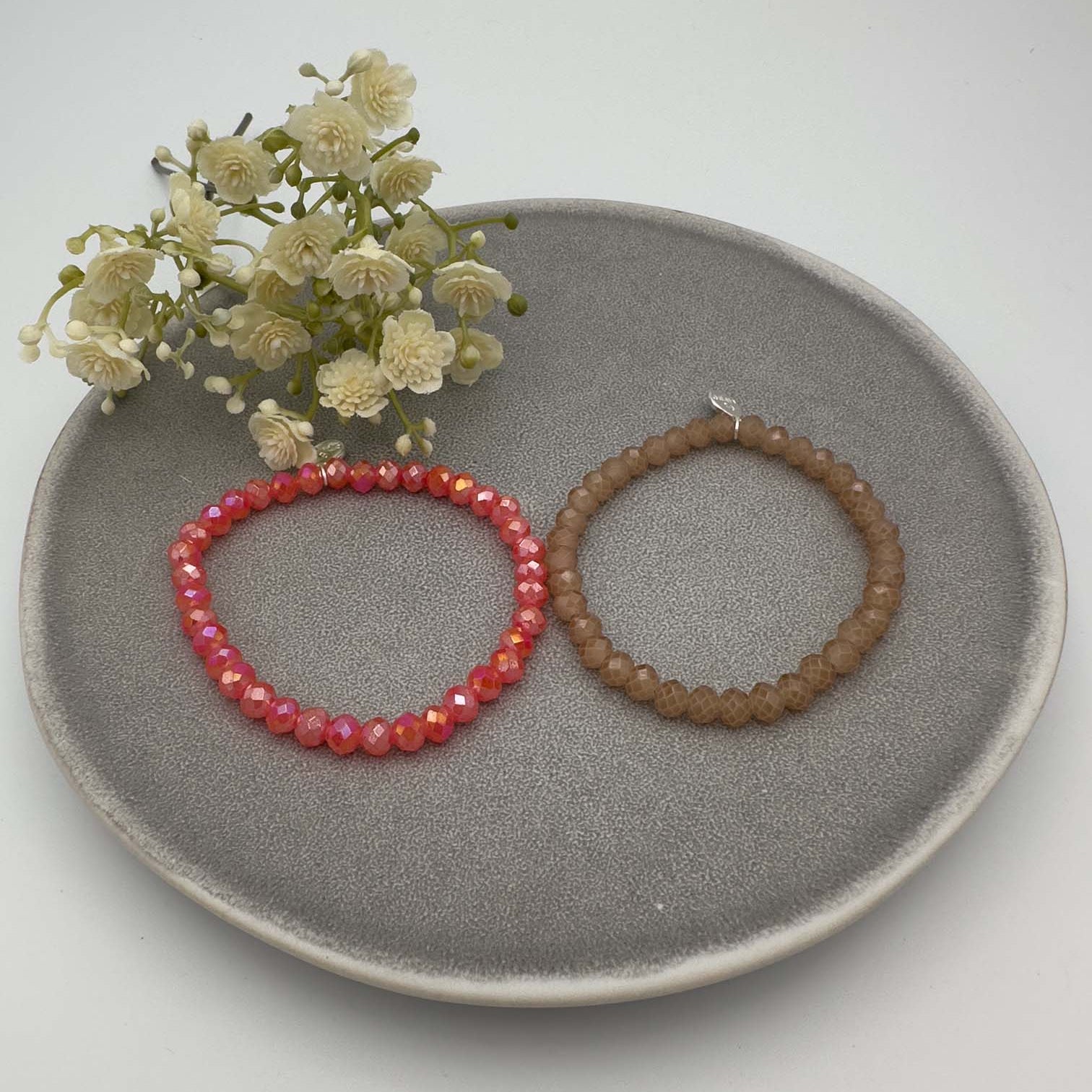 Zwei elastische Perlenarmbaender, eines rot schimmernd und eines braun facettiert.