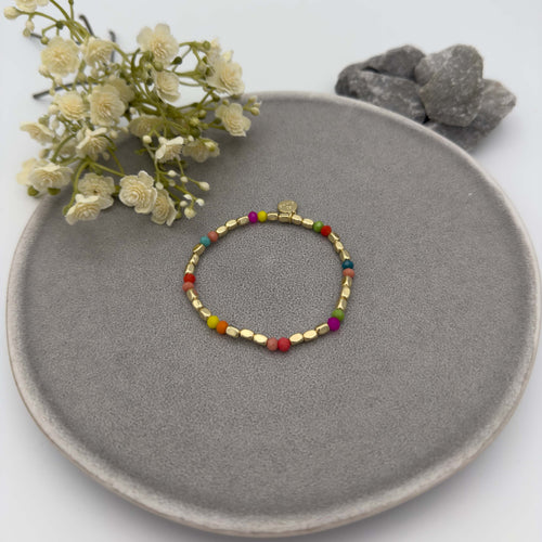 Zartes elastisches Armband mit kleinen goldfarbenen Perlen und einzelnen bunten Perlen in Pink, Gruen, Blau, Gelb und Rot als farbige Highlights