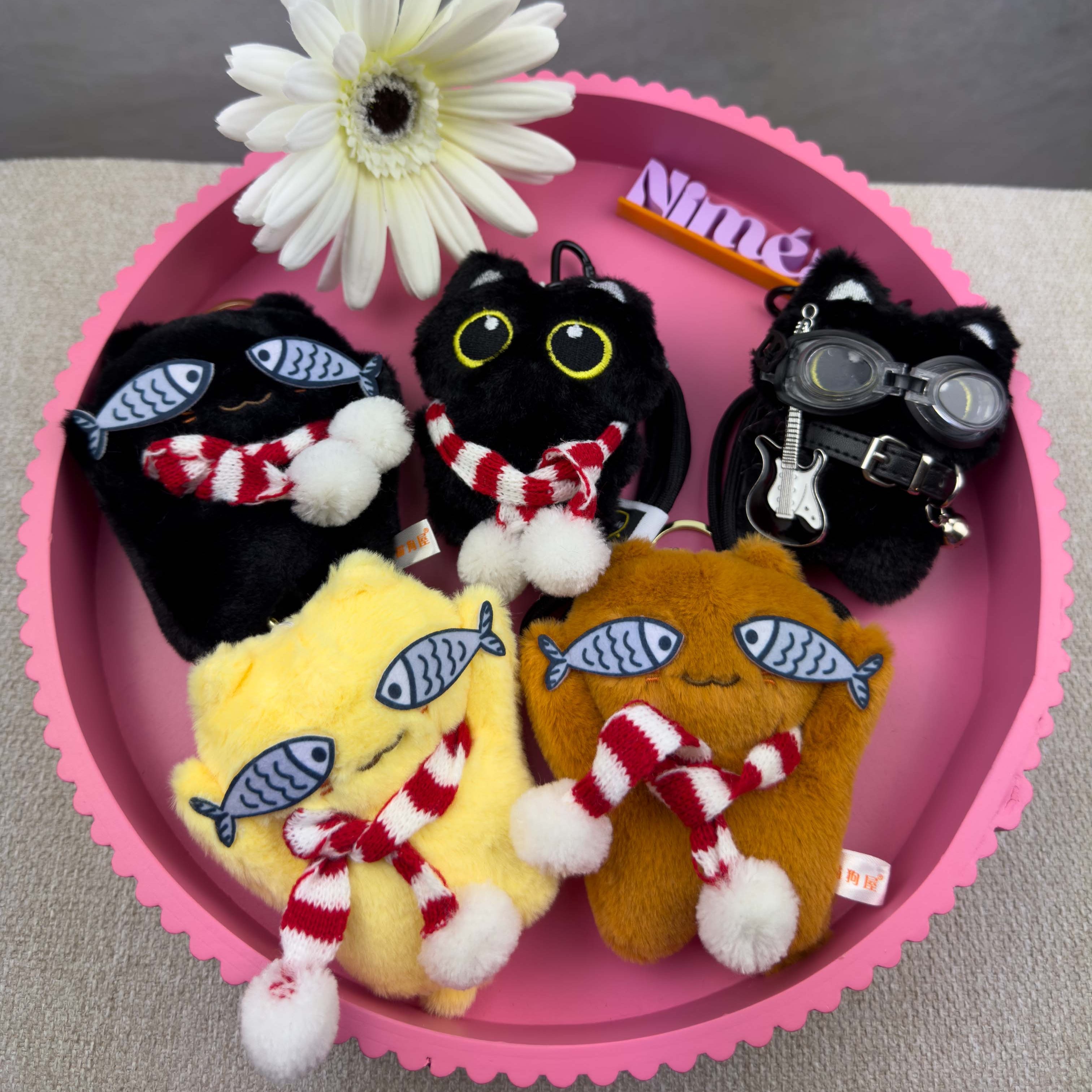 Mehrere flauschige Katzen Schluesselanhaenger in Schwarz, Gelb und Braun mit roten gestreiften Schals und Fisch Motiven sowie unterschiedlichen Details