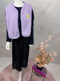 Fliederfarbene Teddy-Weste mit weicher Teddystruktur, Druckknoepfen und gelbem Smiley-Patch auf der Brust.