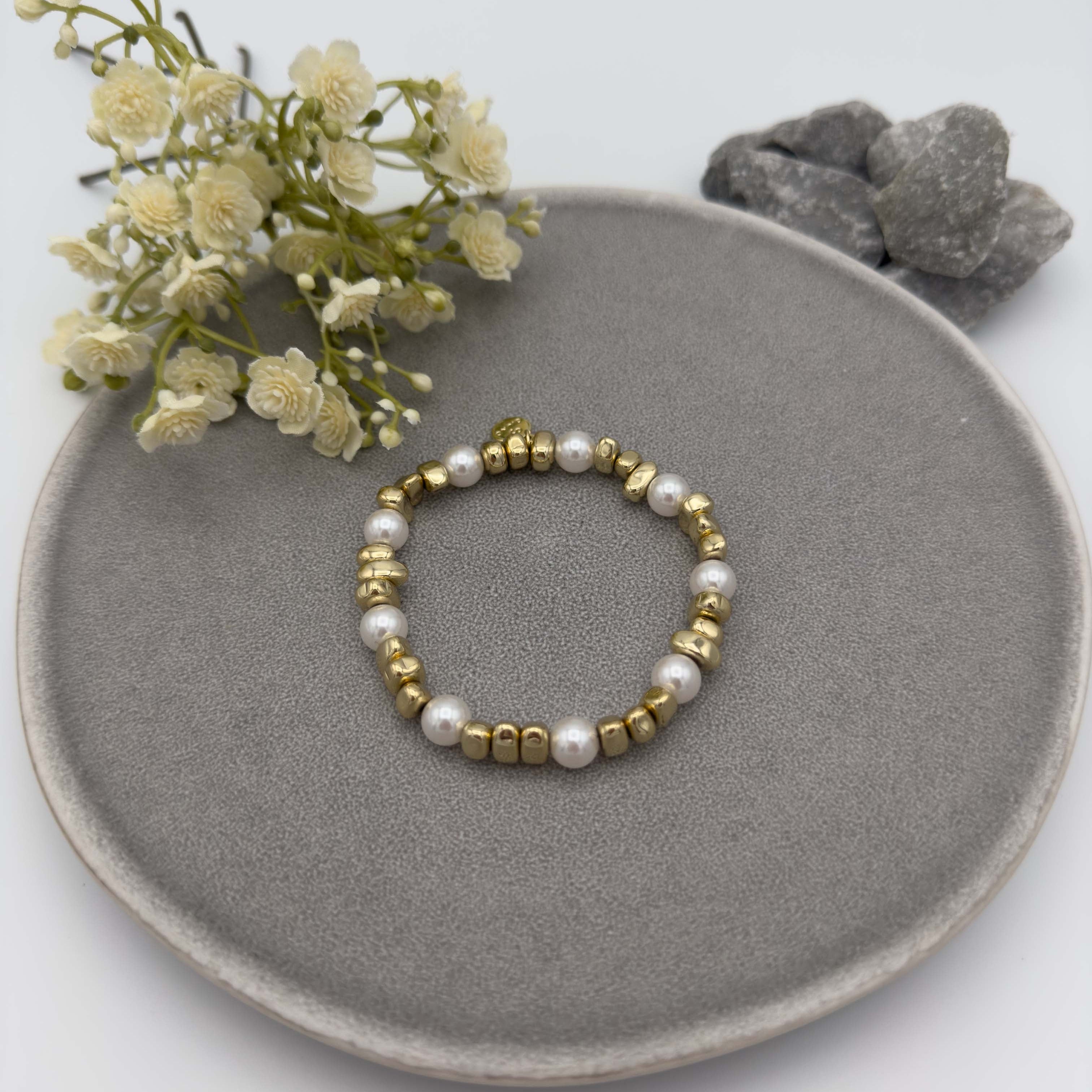Elastisches Armband mit goldfarbenen Metallperlen in unregelmaessiger Form und gleichmaessig verteilten weissen runden Perlen als Akzent.