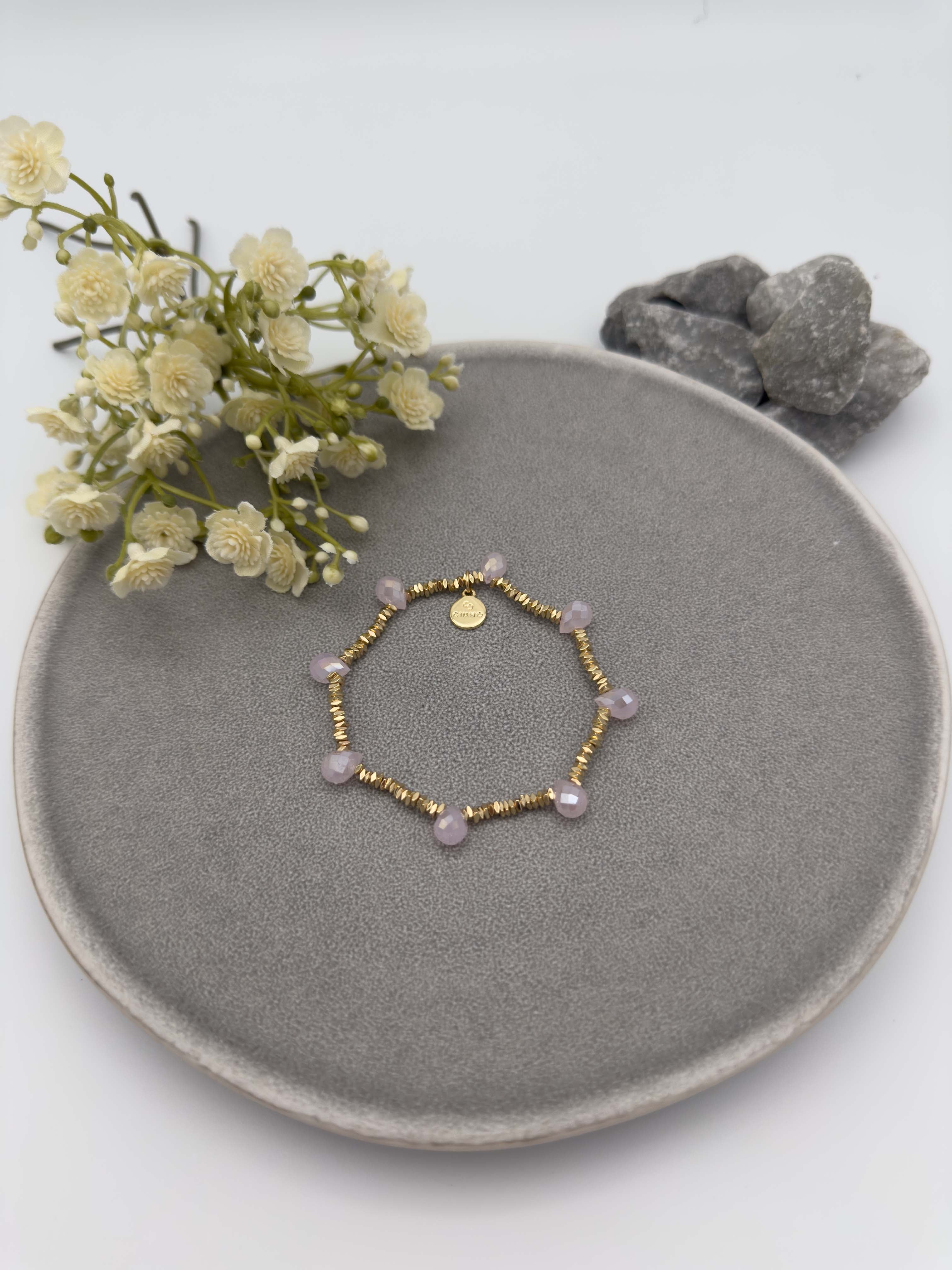 Elastisches goldfarbenes Perlenarmband mit kleinen Metallperlen und gleichmaessig verteilten facettierten rosefarbenen Glasperlen.