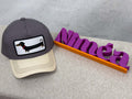 Graue Trucker Cap mit hellem Schirm und aufgenaehtem Patch mit schwarzem Dackel Motiv.
