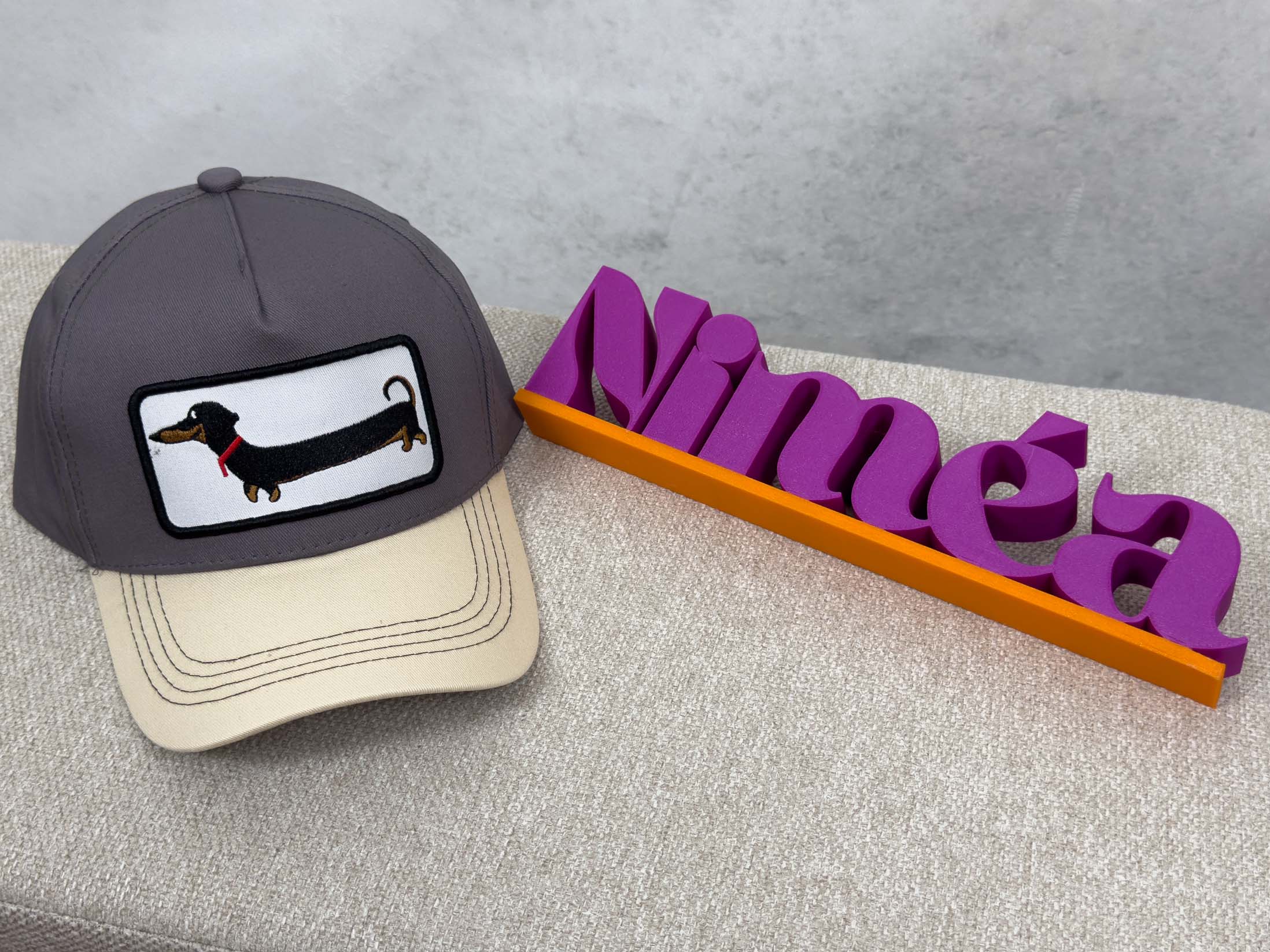 Graue Trucker Cap mit hellem Schirm und aufgenaehtem Patch mit schwarzem Dackel Motiv.