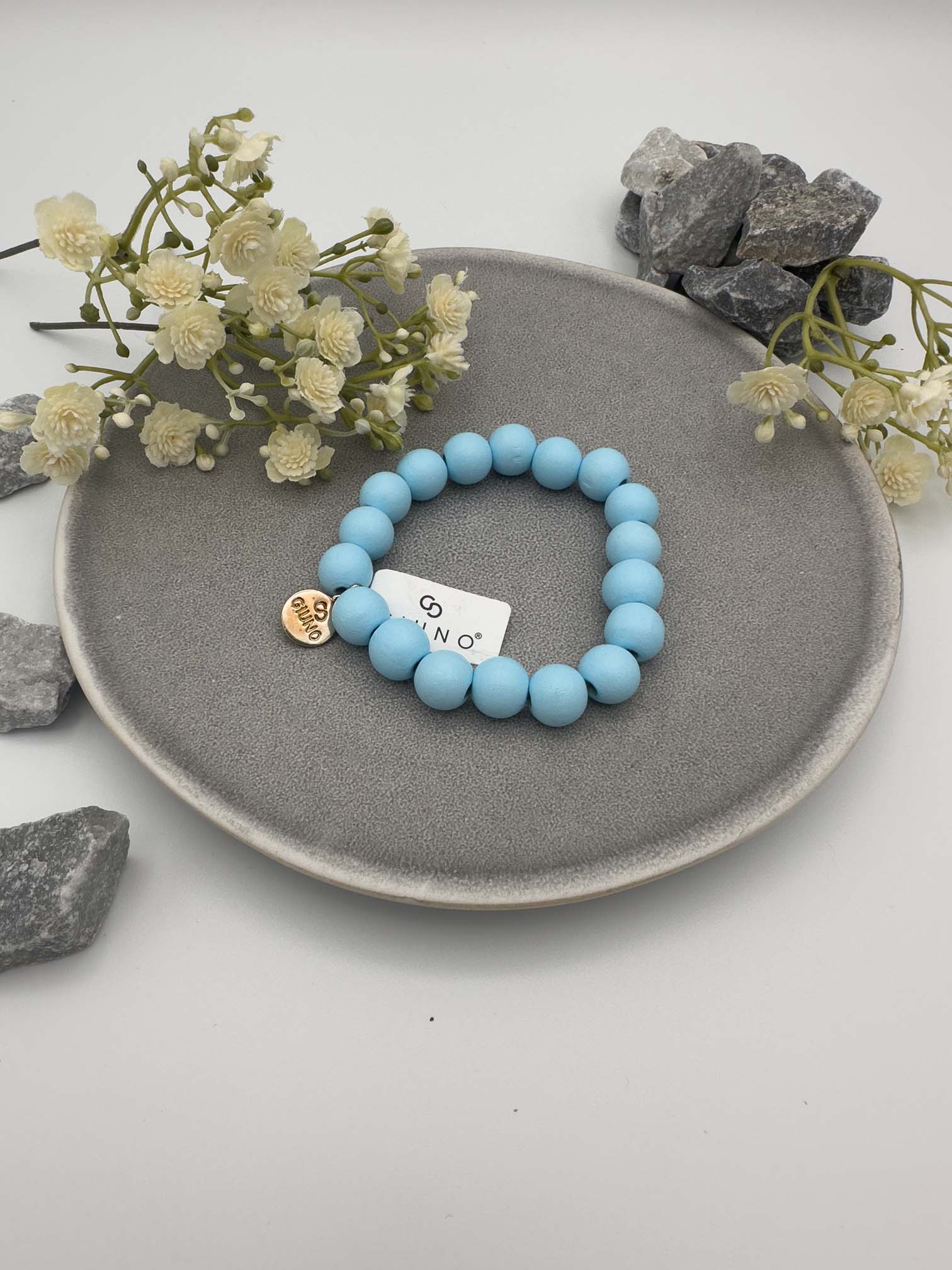 Elastisches Armband aus blaufarbenen Holzperlen mit rundem silbernen Anhänger auf hellem Hintergrund.