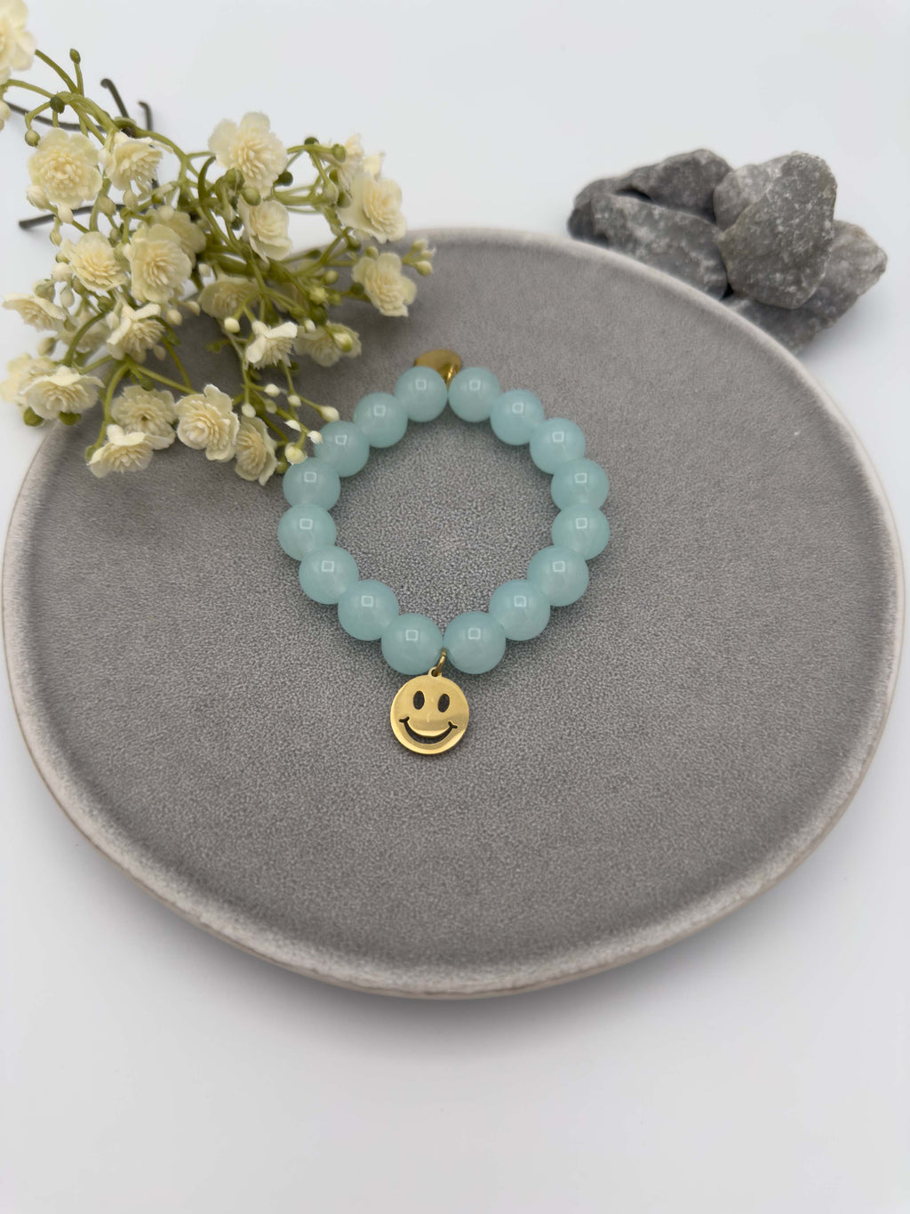 Elastisches Armband mit hellblauen Perlen und goldfarbenem Smiley Anhaenger