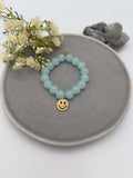 Elastisches Armband mit hellblauen Perlen und goldfarbenem Smiley Anhaenger