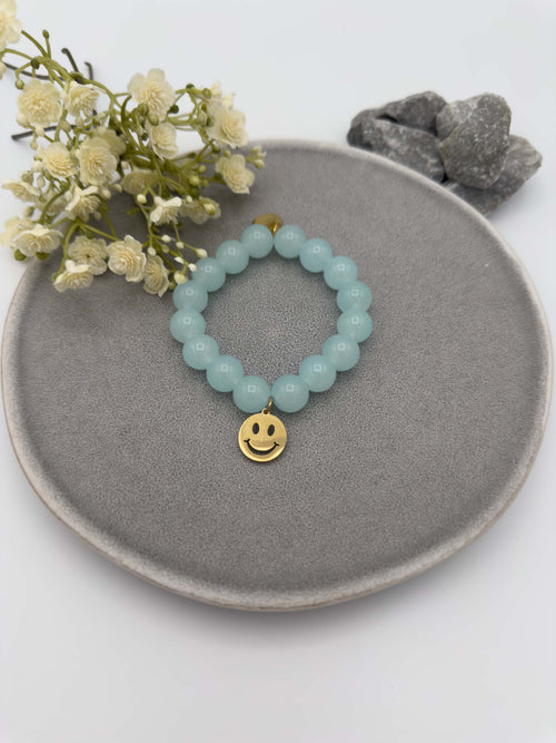 Elastisches Armband mit hellblauen Perlen und goldfarbenem Smiley Anhaenger