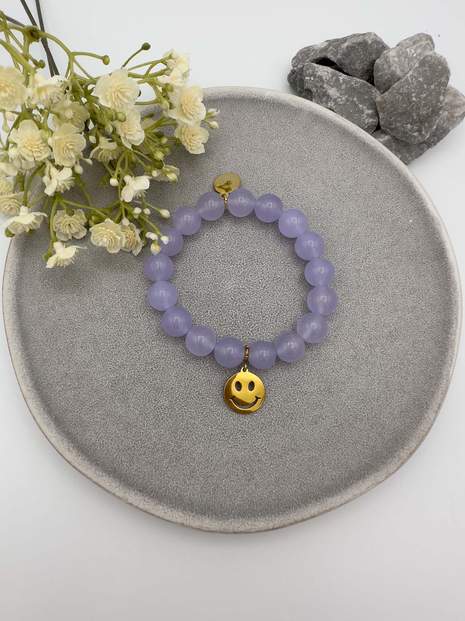 Elastisches Armband mit lila Perlen und goldfarbenem Smiley Anhaenger