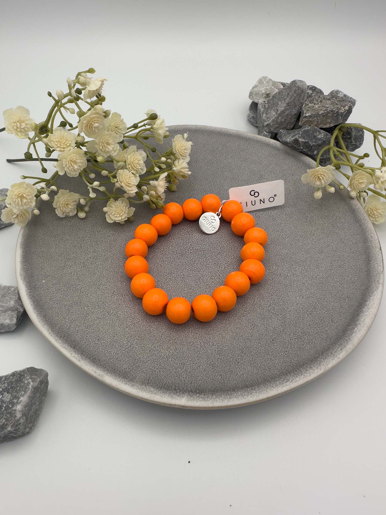 Elastisches Armband aus orangefarbenen Holzperlen mit rundem silbernen Anhänger auf hellem Hintergrund.