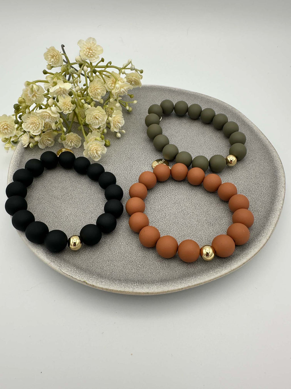 Drei elastische Armbänder mit matten Perlen in Schwarz, Olivgruen und Rostorange jeweils mit goldener Akzentperle