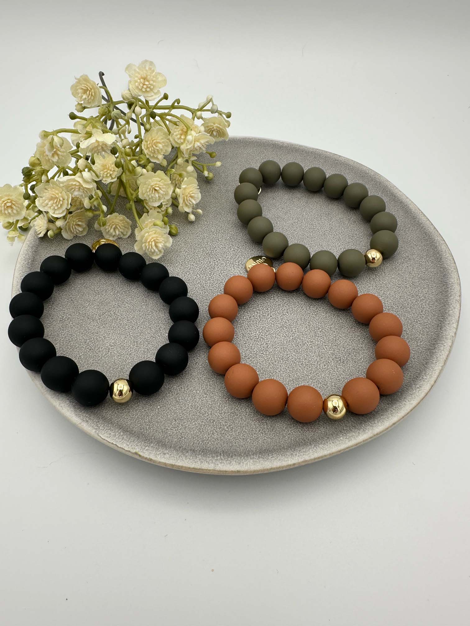 Drei elastische Armbänder mit matten Perlen in Schwarz, Olivgruen und Rostorange jeweils mit goldener Akzentperle
