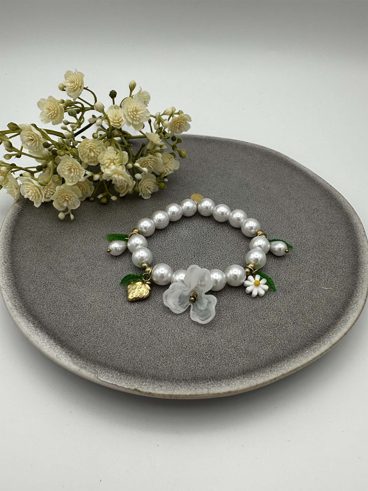 Elastisches Perlenarmband mit weissen Perlen sowie Blumen- und Erdbeeranhaengern
