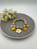 Elastisches Perlenarmband in Beige mit Zitronen-, Blumen- und Fruchtanhaengern in Gelb und Weiss