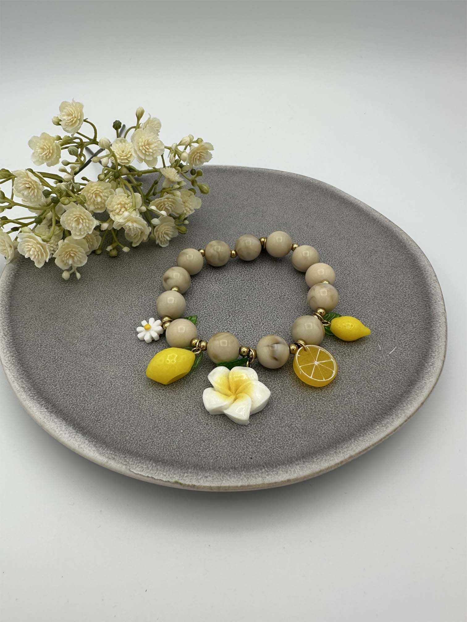 Elastisches Perlenarmband in Beige mit Zitronen-, Blumen- und Fruchtanhaengern in Gelb und Weiss