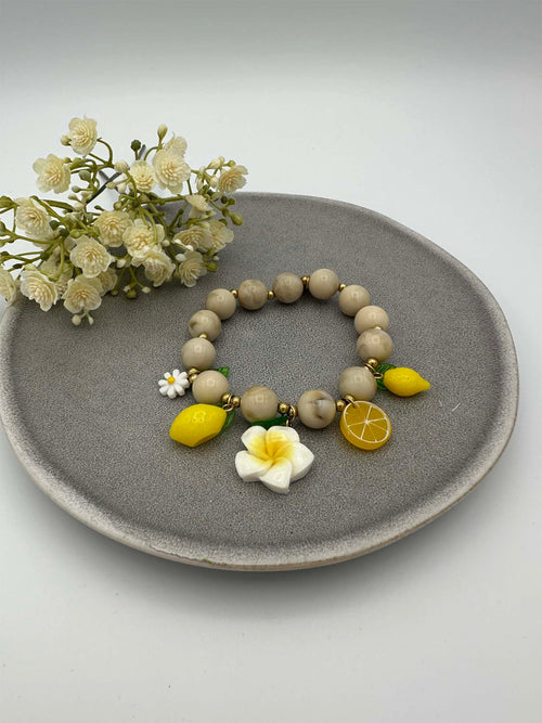 Elastisches Perlenarmband in Beige mit Zitronen-, Blumen- und Fruchtanhaengern in Gelb und Weiss