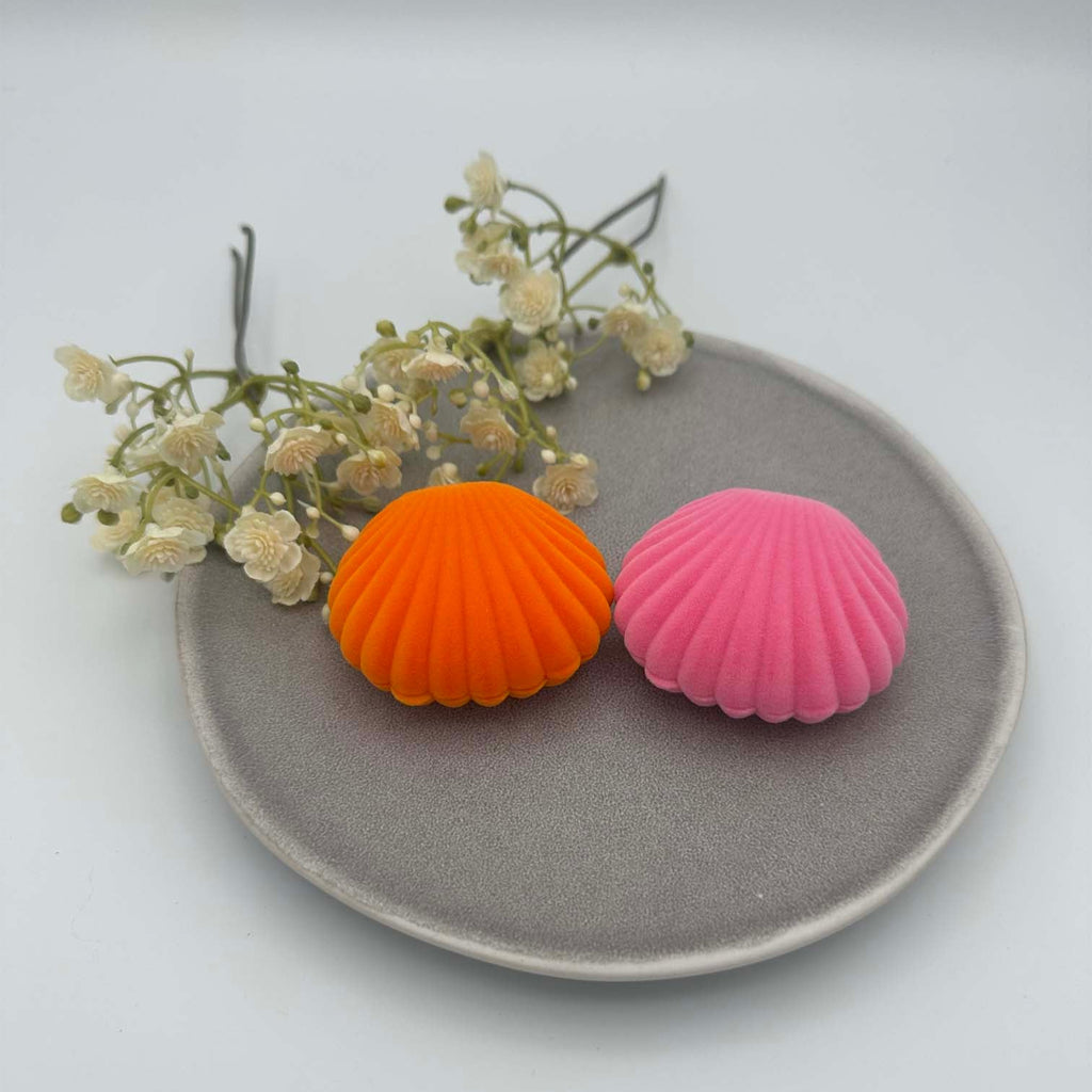 Zwei kleine Schmuckkaestchen in Muschelform aus Samt, eines in kraeftigem Orange und eines in Rosa, geschlossen dargestellt.