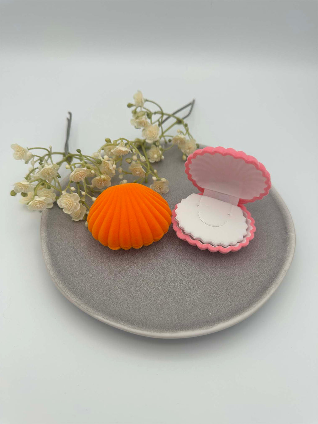 Zwei Schmuckkaestchen in Muschelform aus Samt, eines geschlossen in Orange und eines geoeffnet in Pink mit sichtbarer Innenpolsterung.
