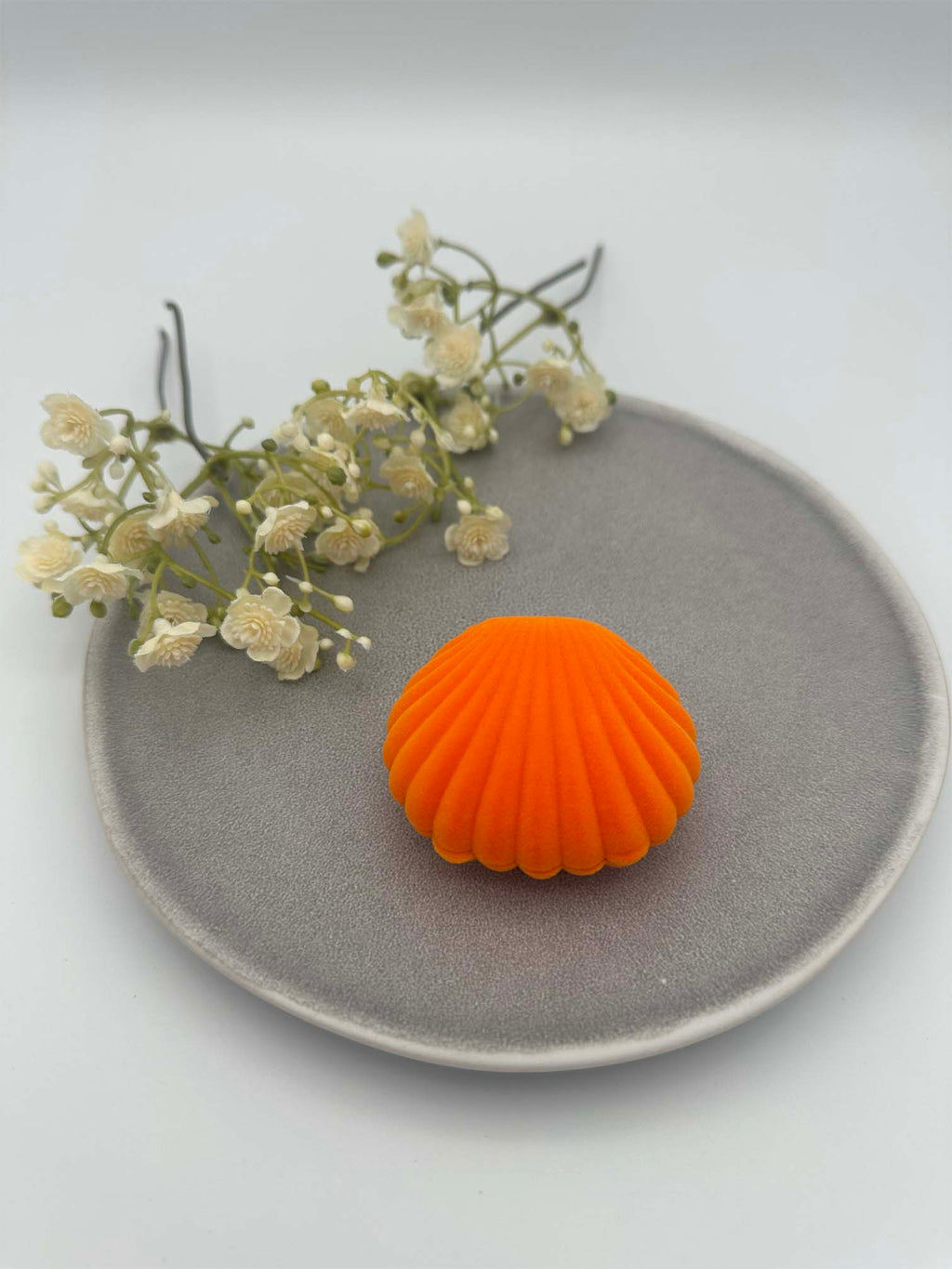 Kleines samtenes Schmuckkaestchen in Muschelform in leuchtendem Orange, geschlossen.