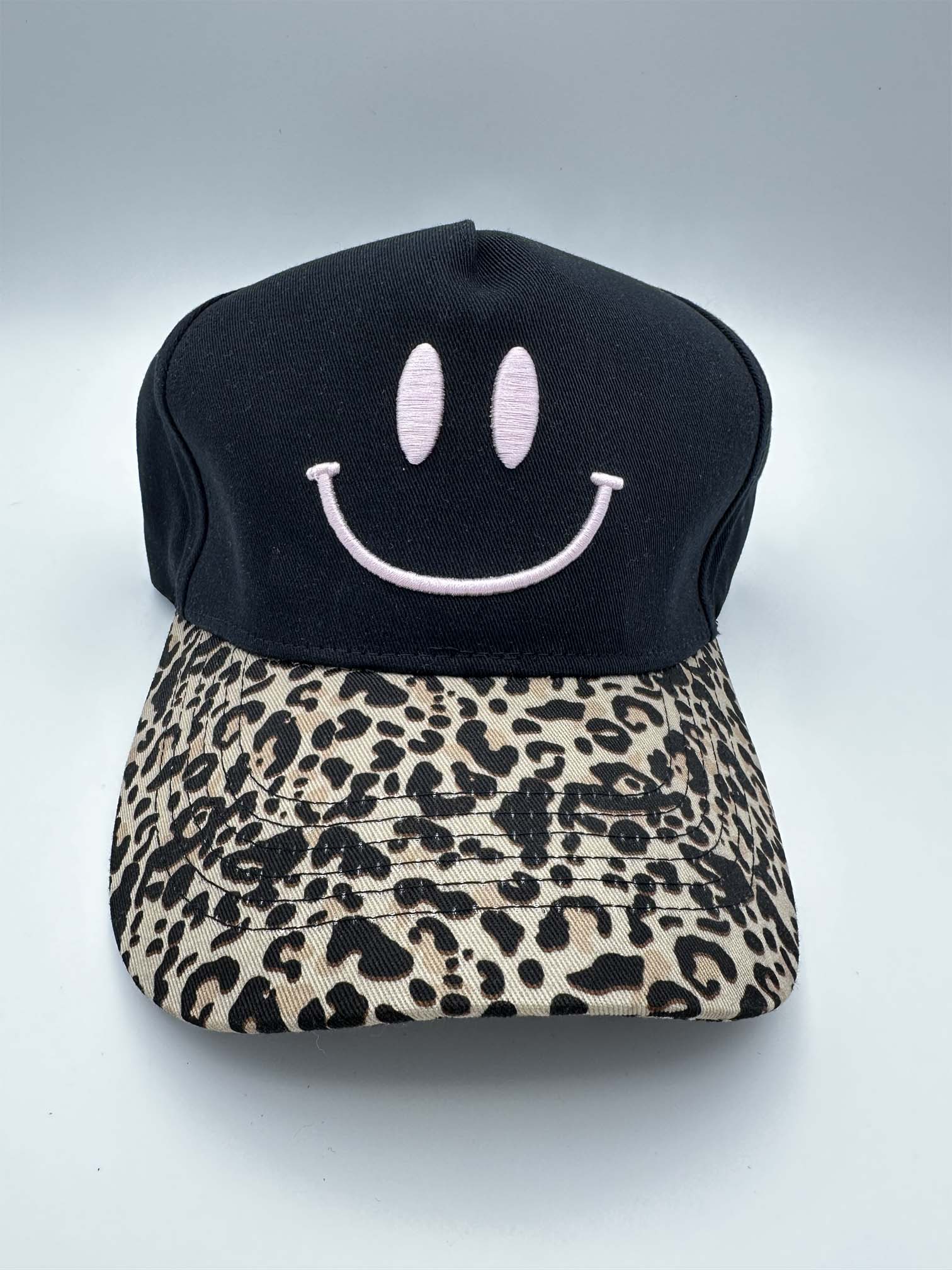 Schwarze Baseball Cap mit rosa gesticktem Smiley auf der Vorderseite und gebogenem Schirm im Leo-Design