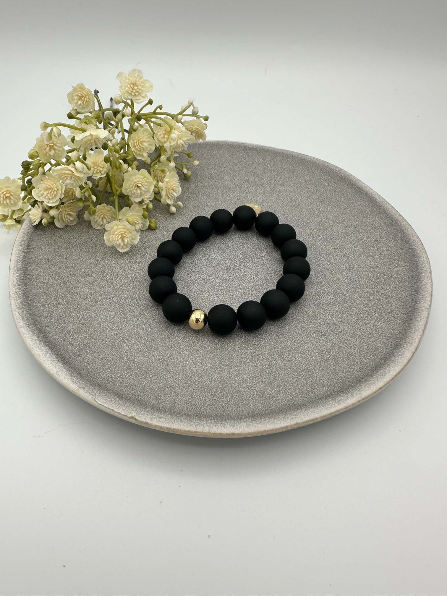 Elastisches Armband mit matten schwarzen Perlen und einer goldenen Kugel