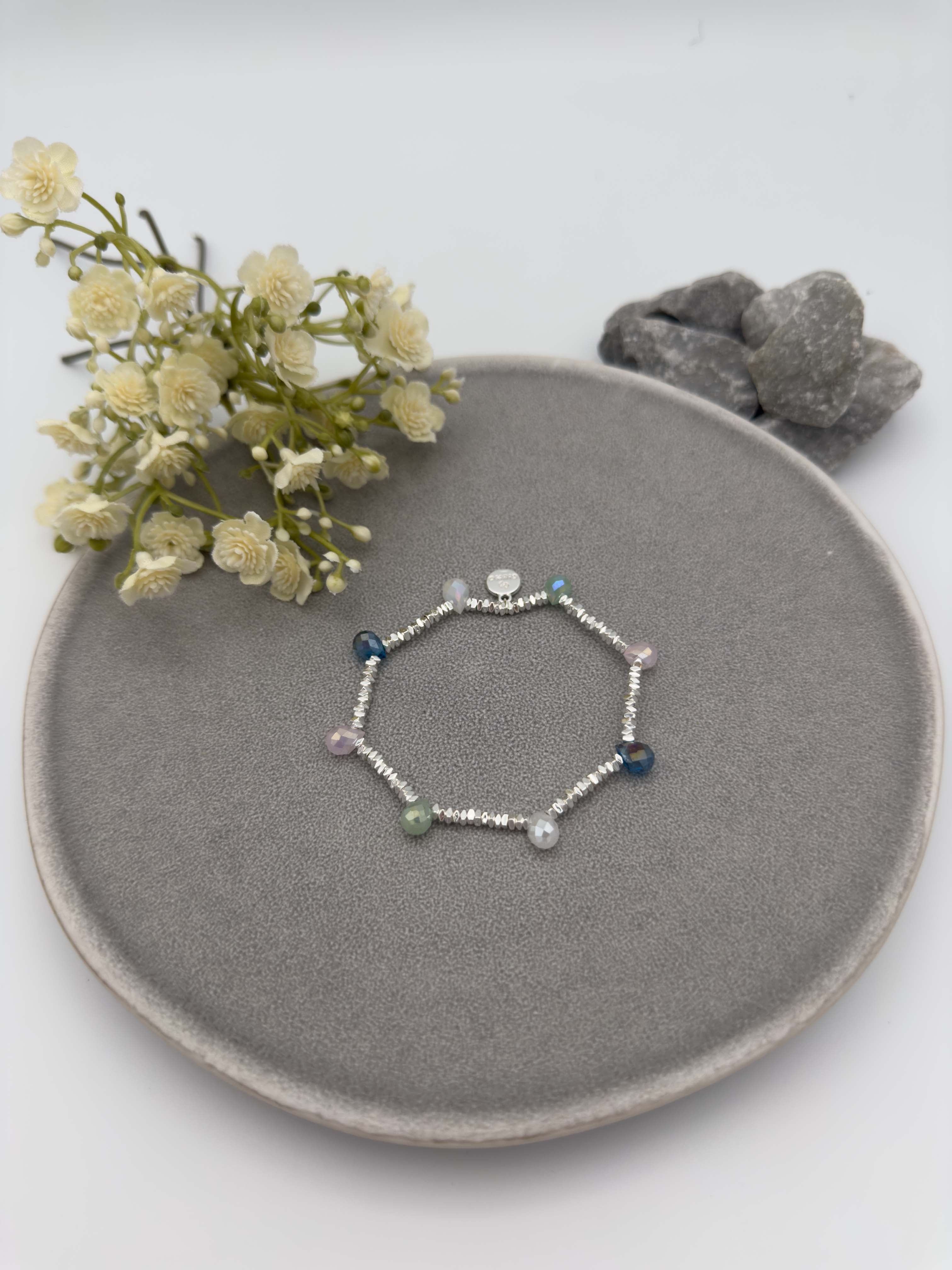 Elastisches silberfarbenes Armband mit schmalen Metallperlen und facettierten Glasperlen in Blau, Gruen, Grau und Rose.
