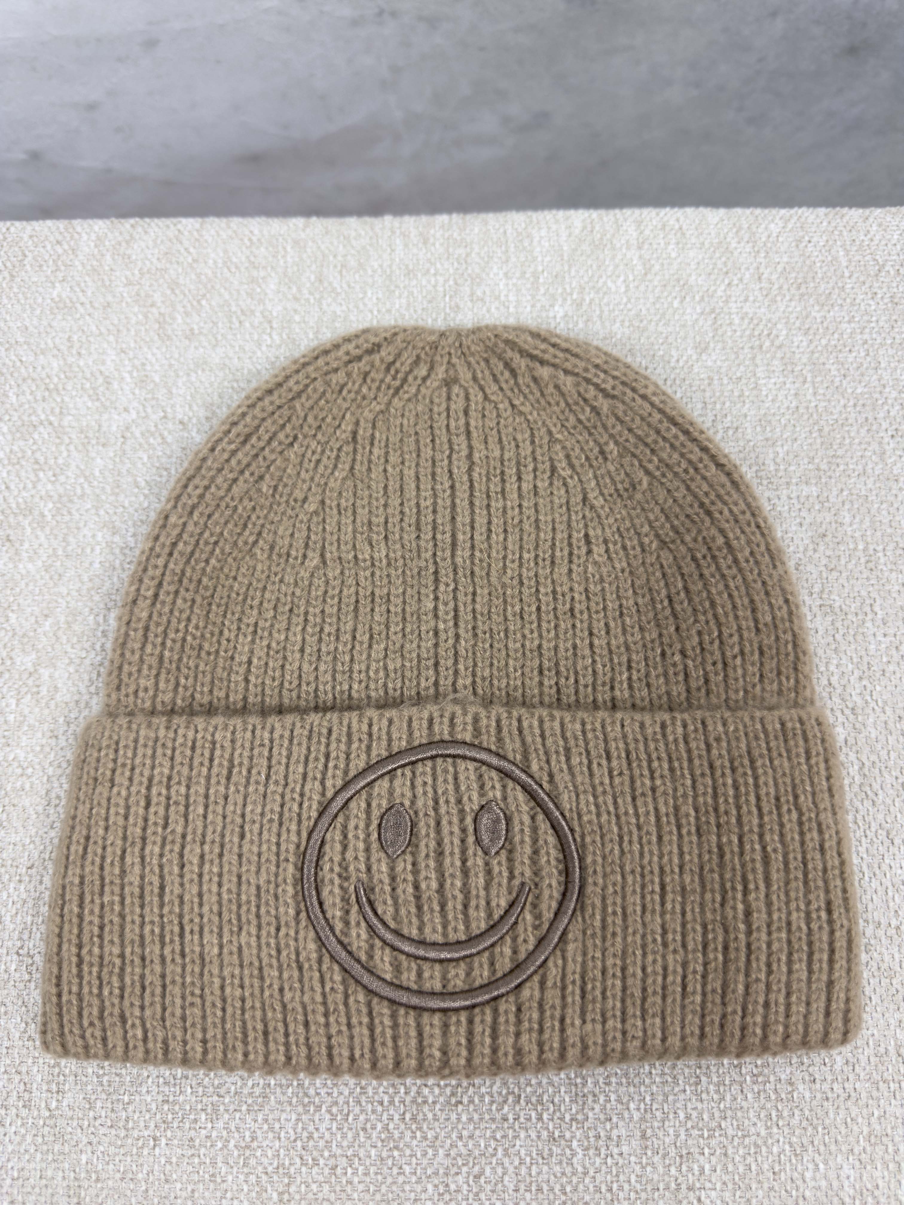 Beige gerippte Strickmuetze mit breitem Umschlag und tonalem Smiley Stick auf der Vorderseite