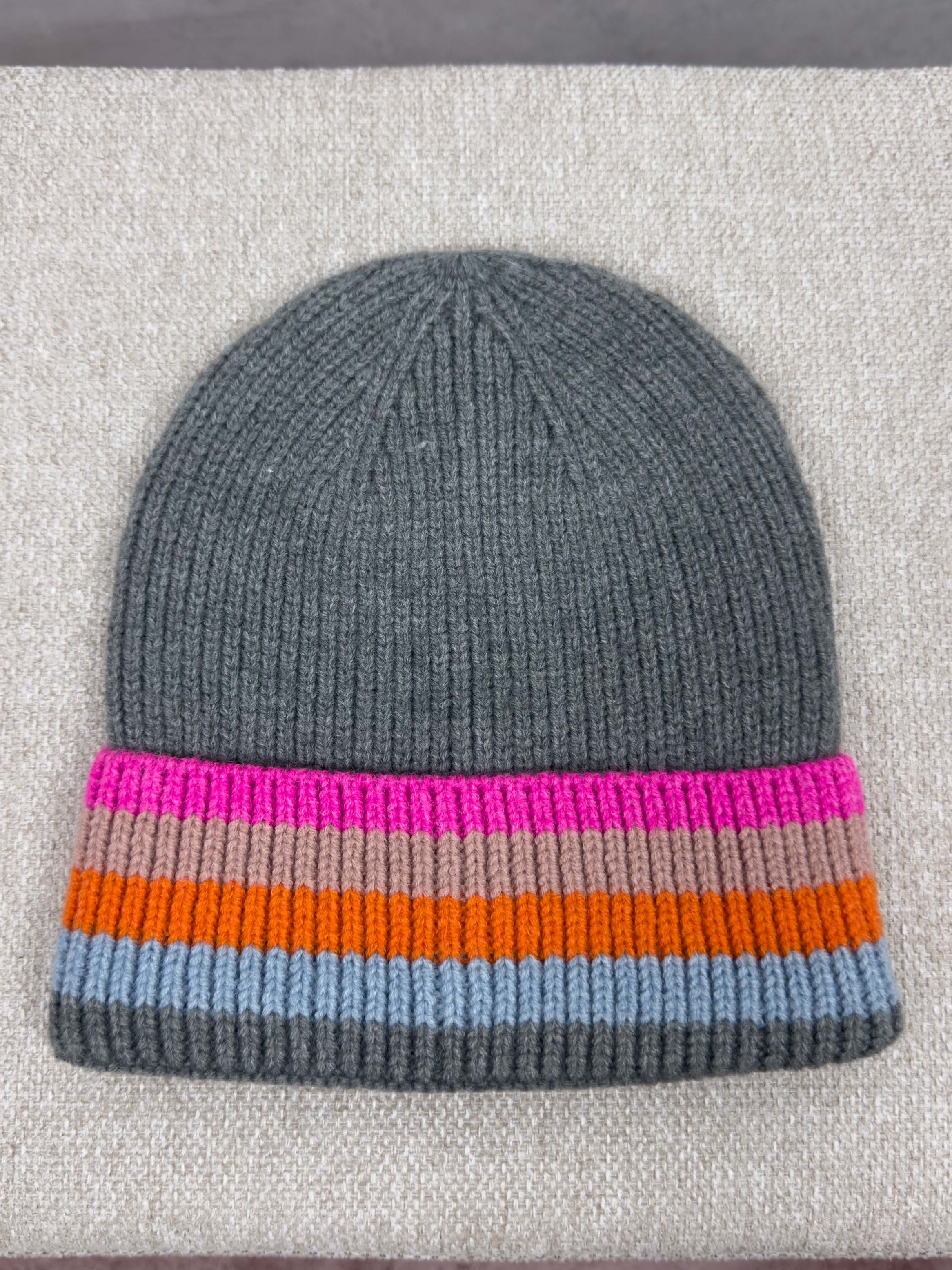 Dunkelgraue Strickmuetze mit geripptem Muster und breitem Umschlag mit Streifen in Pink, Beige, Orange und Hellblau