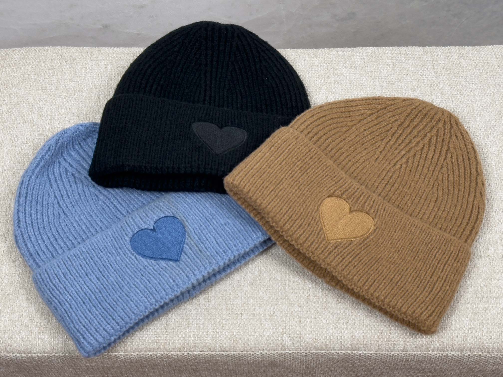 Drei gerippte Strickmuetzen in Schwarz, Camel und Hellblau mit breitem Umschlag und tonaler Herz Applikation auf der Vorderseite