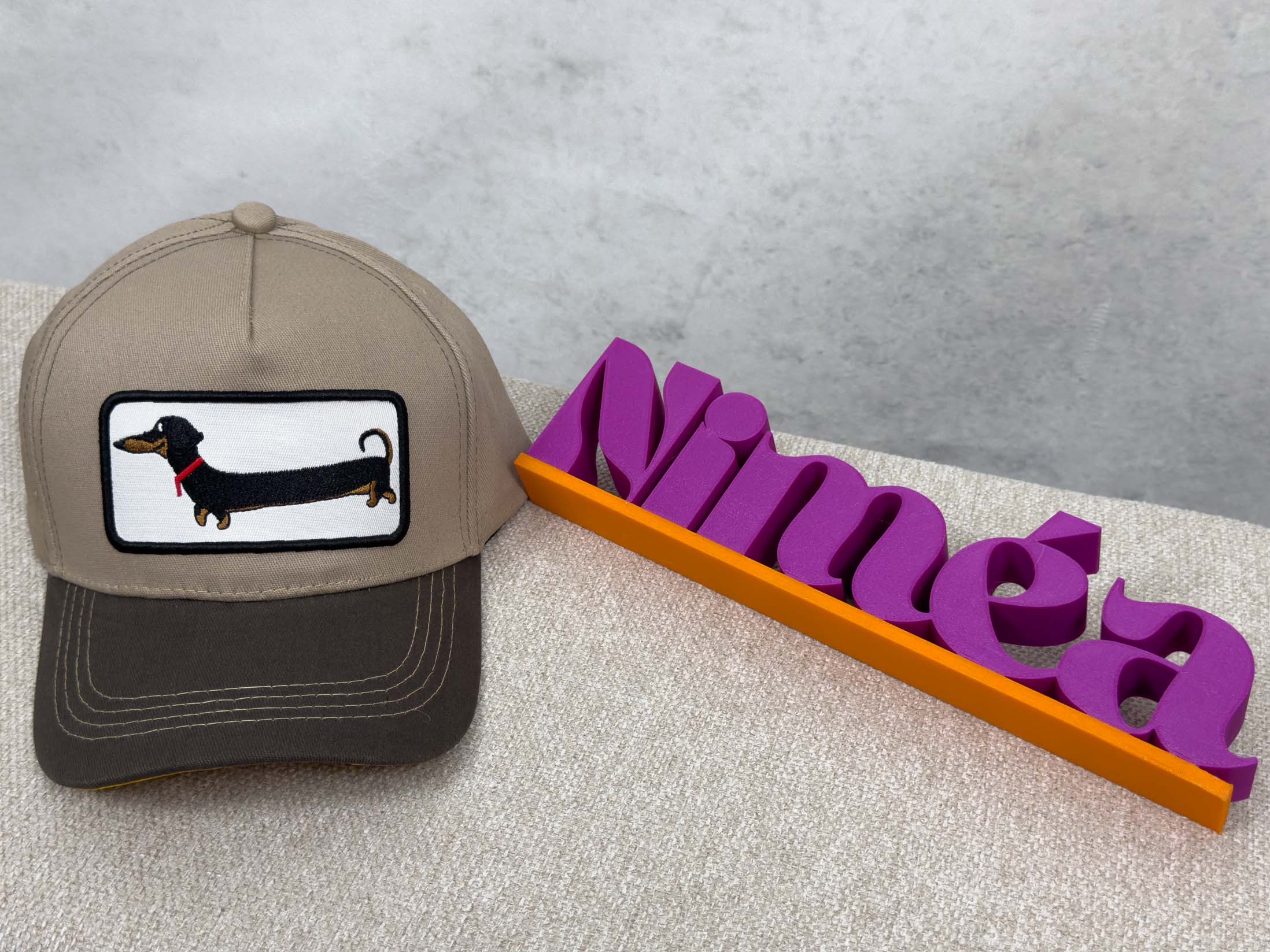 Taupefarbene Cap mit dunklem Schirm und rechteckigem Patch mit gesticktem Dackel.