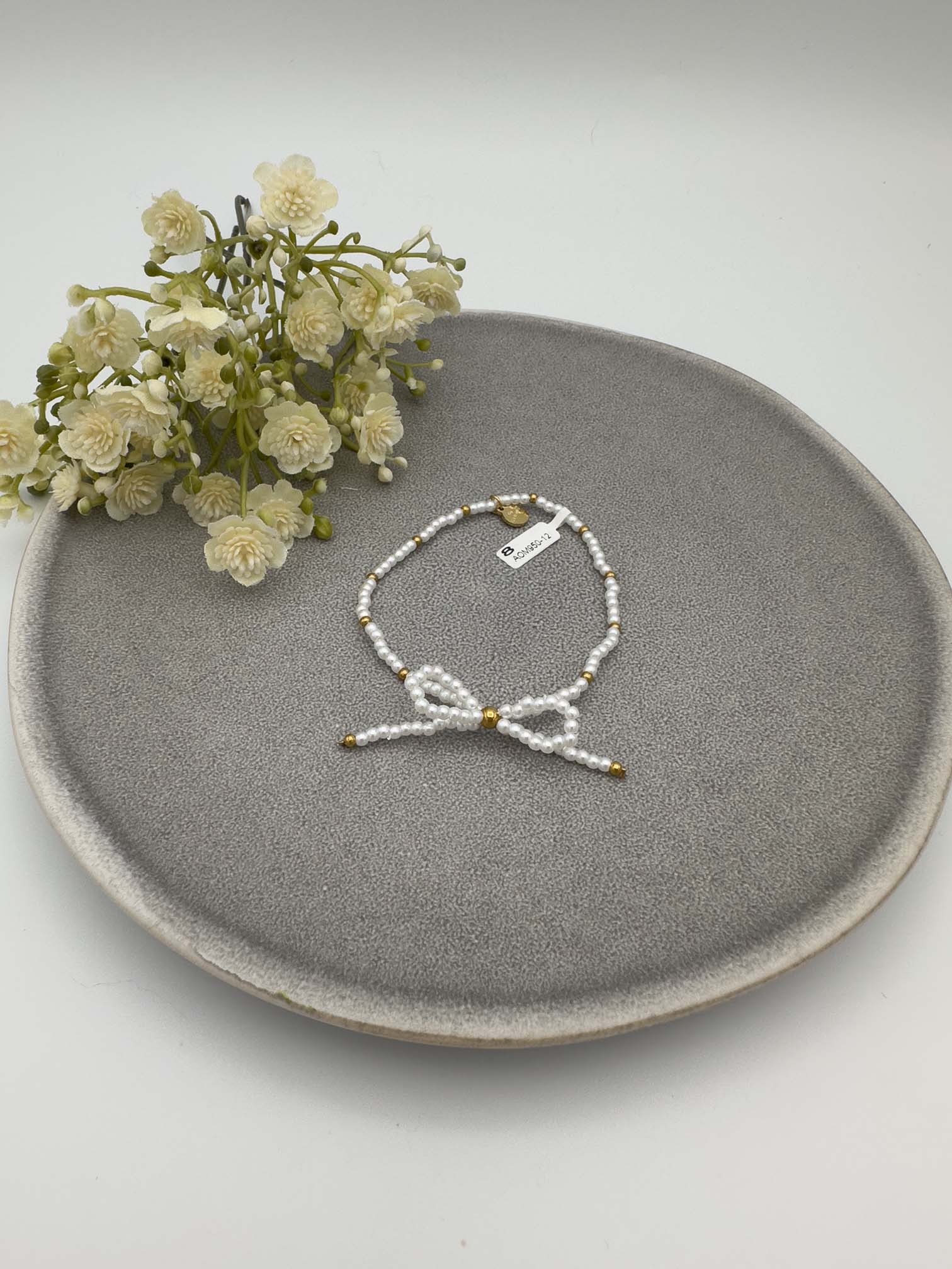 Elastisches Armband aus weißen Perlen mit goldfarbenen Details und Schleife