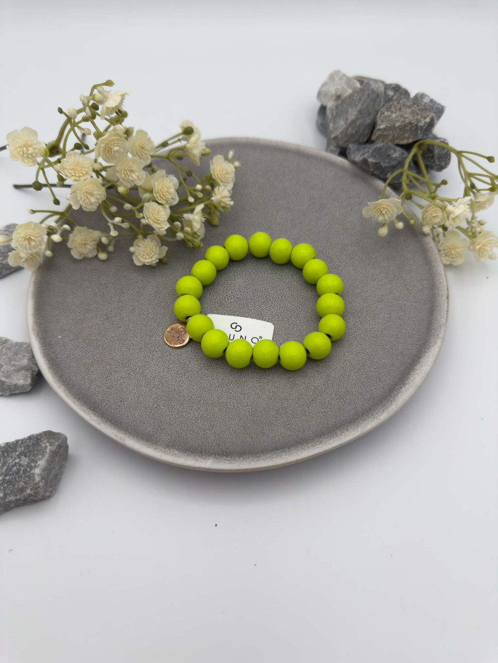 Elastisches Armband aus grünfarbenen Holzperlen mit rundem silbernen Anhänger auf hellem Hintergrund.