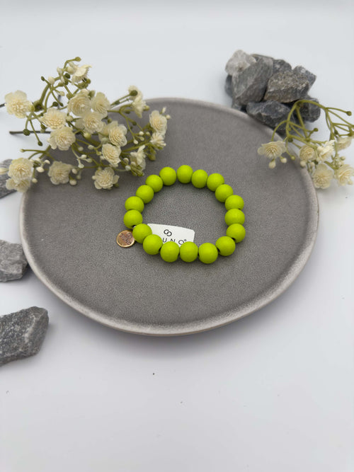 Elastisches Armband aus grünfarbenen Holzperlen mit rundem silbernen Anhänger auf hellem Hintergrund.